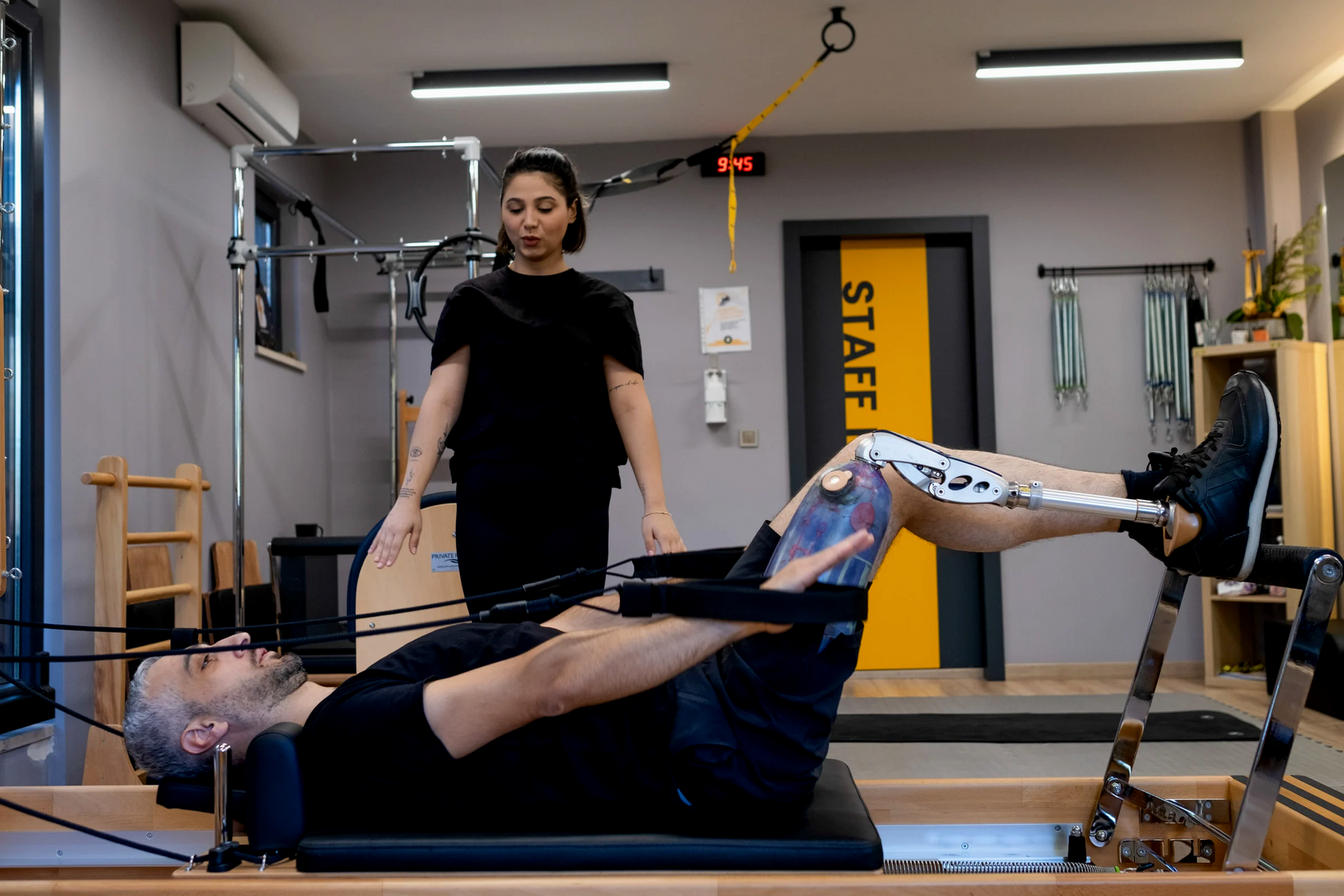 Hombre con pierna prostética haciendo ejercicio de rehabilitación en el suelo mientras es guiado por fisioterapeuta