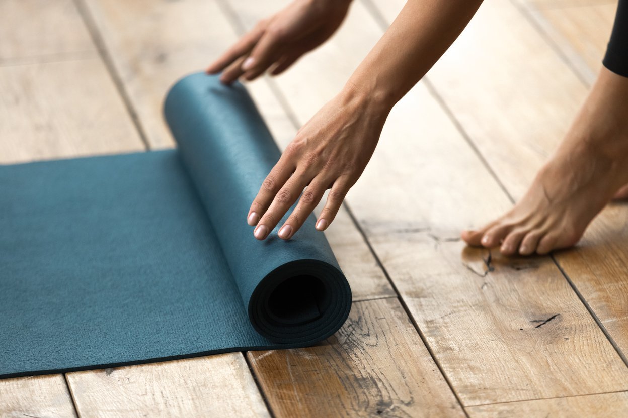 Mujer/hombre desenrollando una esterilla de pilates sobre el suelo